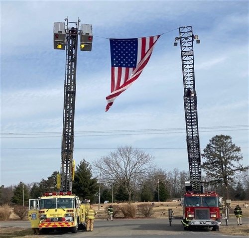 Two ladder trucks raising an American flag