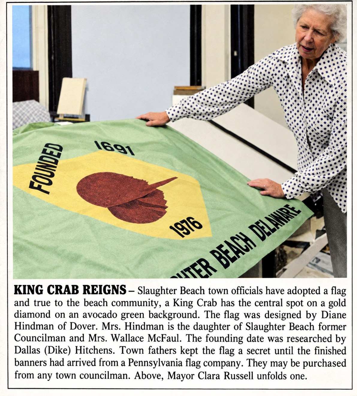 Newspaper clipping headed King Crab Reigns: Mayor Clara Russell unfolds the first Slaughter Beach flag, a horseshoe crab on a gold diamond on an avocado green field, founded 1691, 1976